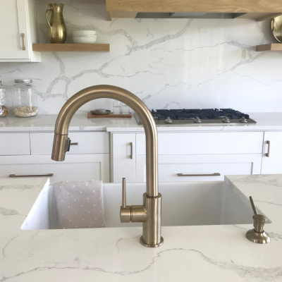 White quartz countertops Orlando with grey veins and gold faucets and farmhouse sink.